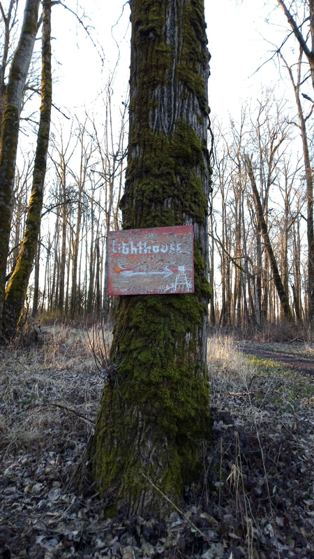 A tree with a custom made, artistic wood sign guiding visitors to the Sauvie Island Lighthouse, February 2022