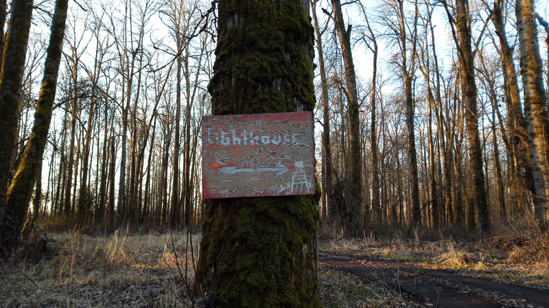 A tree with a custom made, artistic wood sign guiding visitors to the Sauvie Island Lighthouse, February 2022